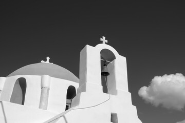 A cross with bells on the top of an orthodox whitewashed church in Ios Greece and a blue sky in the...