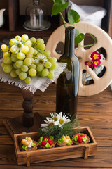 Obraz premium A bottle of wine, cakes and a branch of grapes on display. Wooden wheel in the background, Manor wine cellar