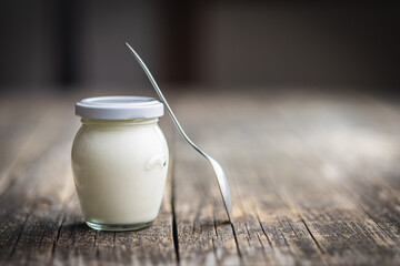 White yogurt in jar on wooden table.