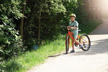Obraz premium a boy in a helmet rides through the park on an orange bicycle . A warm summer day. copy space children bike helmet 