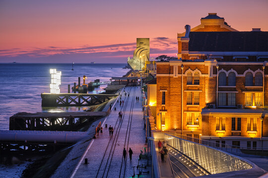 Lisbon, Portugal - August 08, 2022: Electricity Museum in Old Tejo Power Station and Monument to the Discoveries with quay promenade on bank of Tagus river in Lisbom, Portugal illuminated in evening