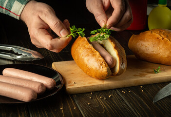 Cooking hot dog on the kitchen table at home. Chef hands add fragrant parsley to hot-dog