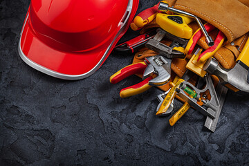 A red Helmet And Construction Tools In Belt On Black Background.