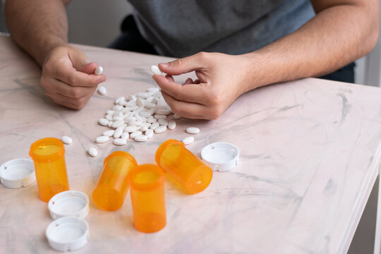 Addicted man taking pills with hands from a lot of medicine drugs on table