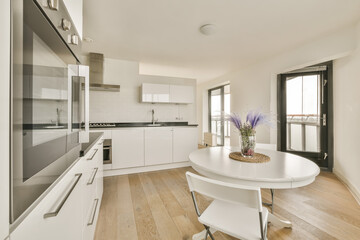 a kitchen and dining area in a modern apartment with white cabinets, wood flooring and an oven on the wall