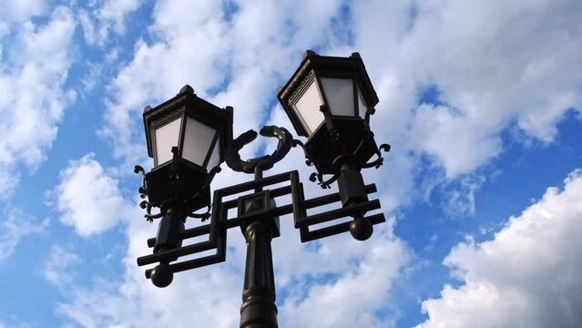 Camera spin around beautiful street lamps in vintage style against blue sky with clouds. Cloudy weather, in foreground are retro old lanterns on pole in center of old city.