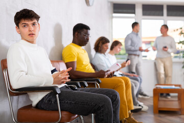 Fototapeta premium Emotional young guy sitting in lobby of government agency with indignant expression, waiting for clerk consultation..