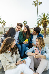 Multiracial group of young friends with mobile phone enjoying a day off social meeting outdoors. Millennial generation people relaxing together outdoors while talking and laughing. Youth community