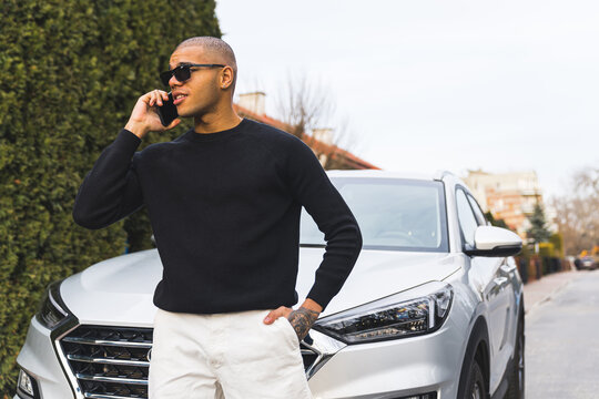 Handsome black young man on a call with his girlfriend near his luxury car on street. High quality photo
