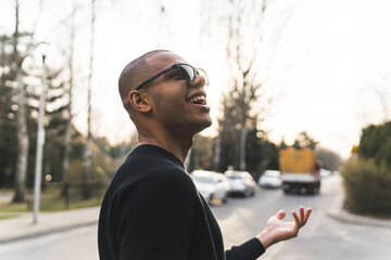 African American smiling man in sunglasses standing on street gestures with hand. High quality photo