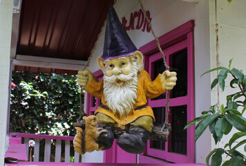 Figura de Duende en columpio con gorro morado, camisa amarilla, pantalón café y barba blanca con una ardilla en su bota. 