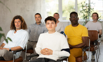 Group of focused men attentively listens to a lecture on same-sex relationships, sitting on chairs in the audience