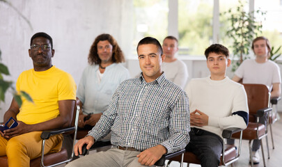 Smiling happy man participating in study session, sitting in auditorium with male group and...