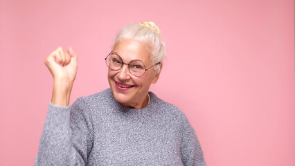 An elderly European woman in glasses confidently looks into the camera, smiling