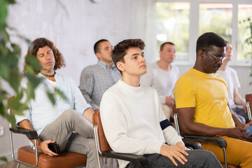Attentive men participants of training listening lecturer sitting on chairs lined up in auditorium