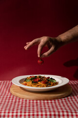 hand holding pepper over arrabiata pasta on red background