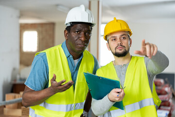 Two builders, african-american and european men, discussing working plan in apartment during repair works.