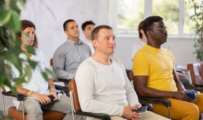 Group of focused men attentively listens to a lecture on same-sex relationships, sitting on chairs in the audience