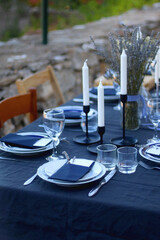 Table setting with white and blue dishes, candles and lavender flowers. Rustic Mediterranean style. Selective focus.