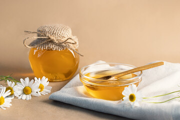 Chamomile syrup in a small bowl and in a jar and chamomile flowers on a linen kitchen towel, copy space