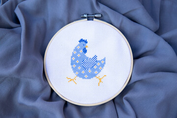 A beautiful cross-stitched blue cockerel in a flower. Embroidered bird on fabric