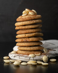 Stacked white chocolate and macadamia nut cookies on white cloth with a dark background