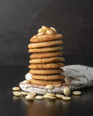 Stacked white chocolate and macadamia nut cookies on white cloth with a dark background