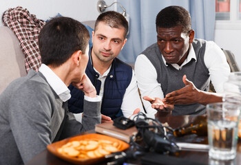 Caring friends calming distressed guy sitting together in home interior