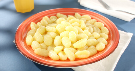 Potato gnocchi on a red plate on a blue background. Close-up. Angle view. Camera tracking. Italian cuisine. Cooked food. Sunny day.