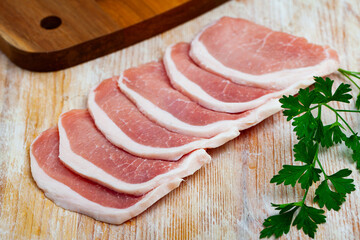 Raw thin pork chops on wooden surface with fresh parsley. Main ingredient for cooking