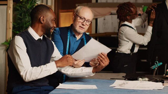 Senior couturier using meter to take measurements for client order, ensuring perfect size for custom made suit. Luxury tailor with measuring tape manufacturing handmade clothes. Handheld shot.