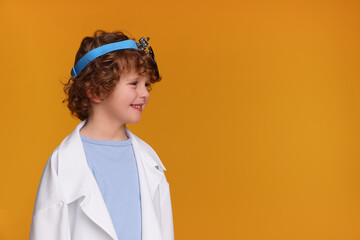 Little boy in medical uniform with head mirror on yellow background. Space for text