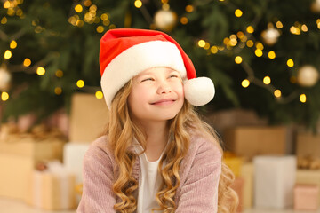 Cute little girl wearing Christmas hat near tree and gifts at home - Powered by Adobe