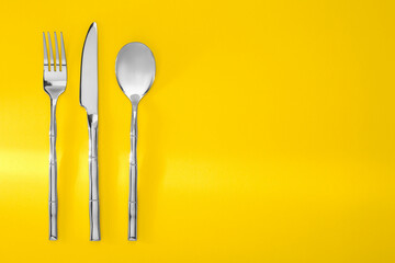 Spoon, fork and knife on yellow background, flat lay. Space for text