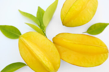 Delicious ripe carambolas with green leaves on white background