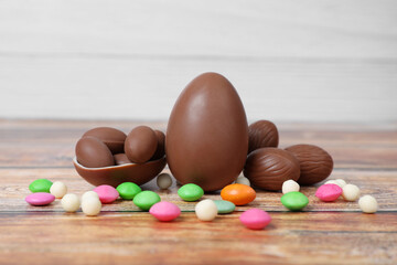 Delicious chocolate eggs and colorful candies on wooden table