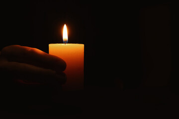 Woman holding burning candle in hand on black background, closeup. Space for text