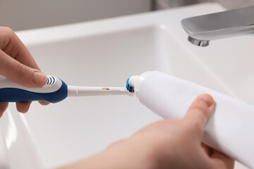 Woman squeezing toothpaste from tube onto toothbrush above sink in bathroom, closeup