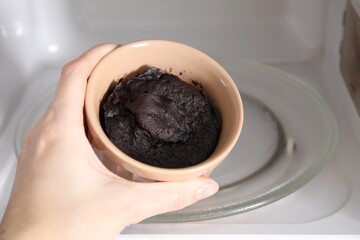 Woman taking ramekin with tasty chocolate pie out of microwave, closeup. Cooking cake