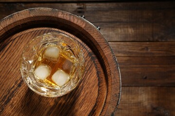 Glass of whiskey and barrel on wooden background, top view. Space for text