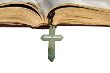 A jade crucifix cross hanging down from an open bible. Isolated, transparent background.