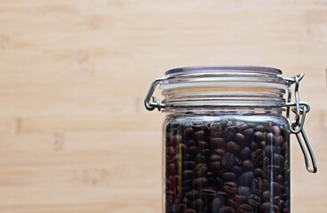 Black coffee beans are packed in clear glass bottles with wood grain background.