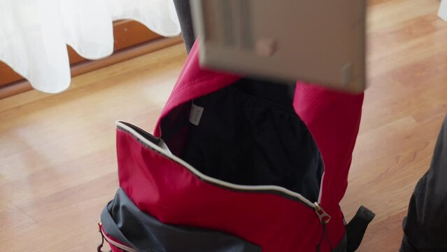 Packing books into red back pack and zipping it, ready for school