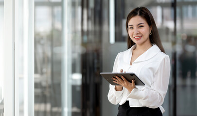 Fototapeta na wymiar Young Asian businesswoman looking at camera holding tablet at office.