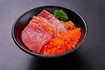 Top view of Sashimi Set (Bluefin Tuna, Raw Salmon, Hamachi, Uni and tobiko) sliced and top with white sesame, put together in a black bowl and ready to served. Popular Japanese food.