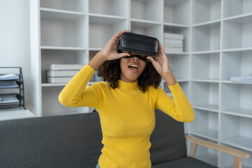 Stylish cheerful african american woman in vr headset spread arms and smiling while dancing and raising fingers in cyberspace. Metaverse vr future girl concept.