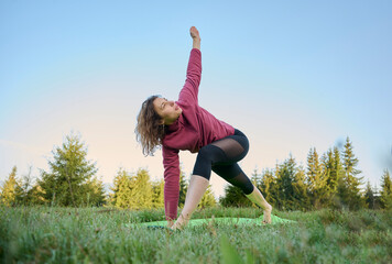 A young yogi woman is doing yoga outdoors on a meadow in the mountains with a beautiful background