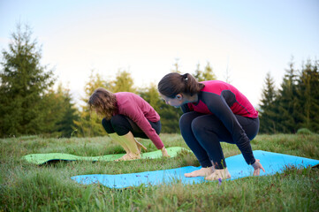 Two athletic young women dressed in sporty attire engage in a range of yoga poses amidst the scenic...