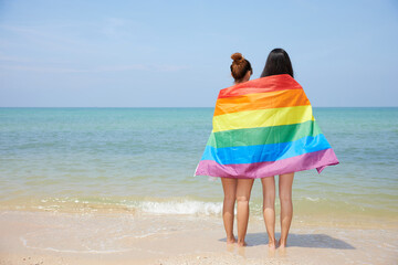 back lesbian couple with a rainbow flag on the beach