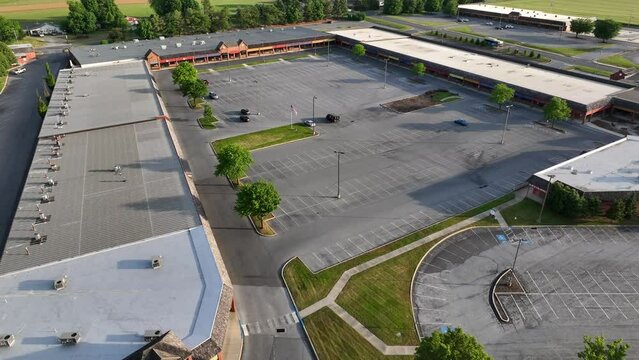 Desolate shopping center in USA. American flag waving in empty parking lot of outlets. Deserted retail store space theme.